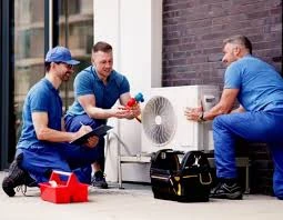 Three HVAC technicians working together on an outdoor air conditioning unit