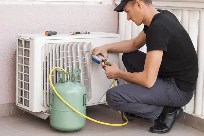 Technician servicing a residential cooling unit with a gauge and refrigerant cylinder